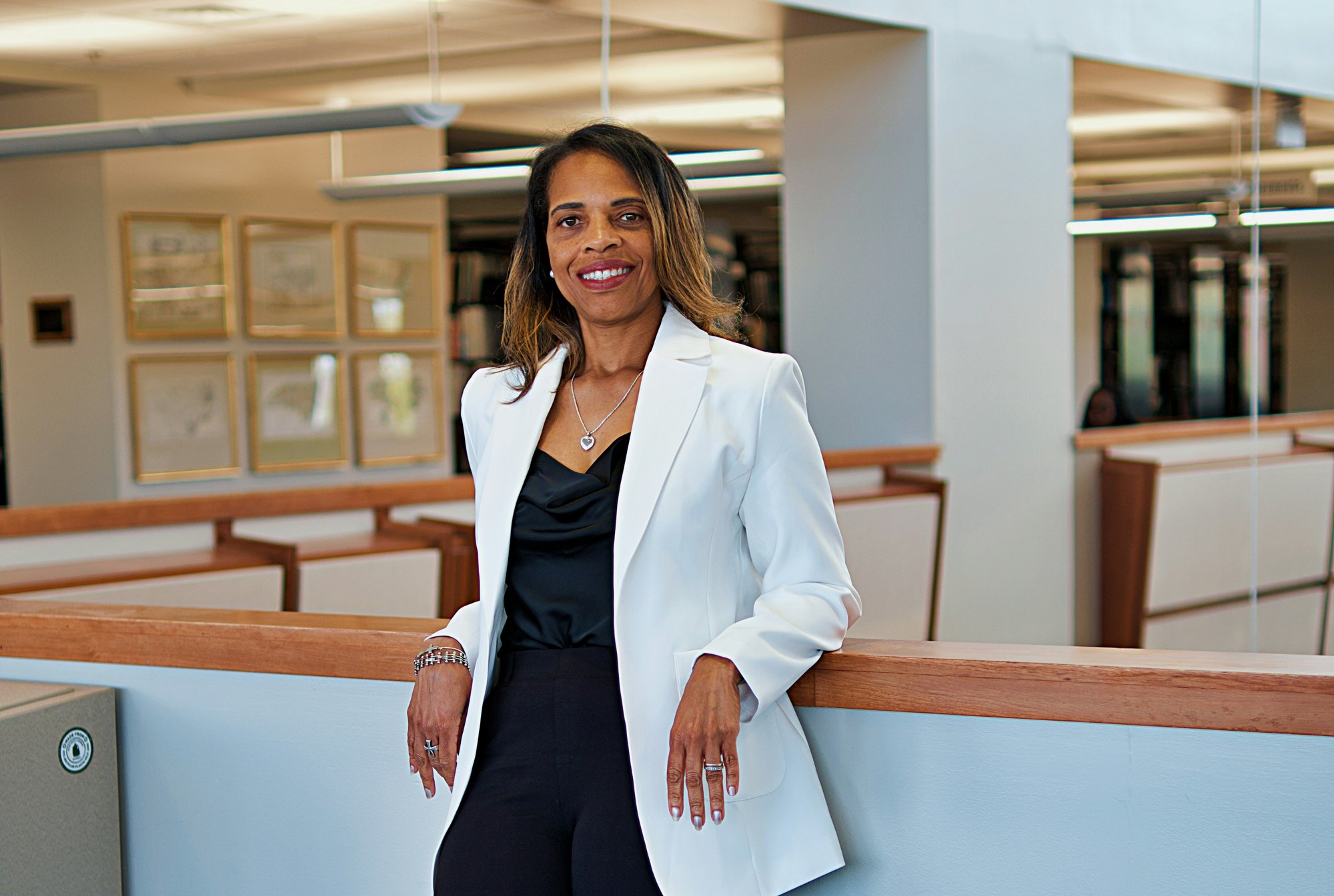Smiling business leader in a white blazer leaning on a railing in a bright modern office